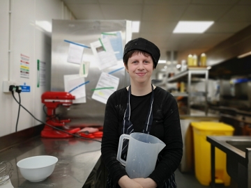 A smiling young woman holding jug in cafe kitchen